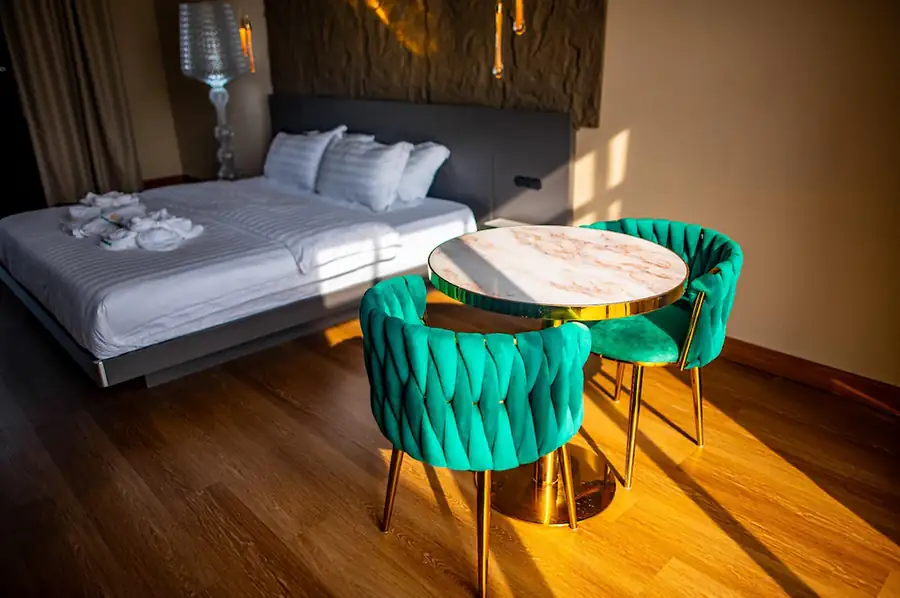 Sunlight illuminating a stylish marble table and teal velvet chairs next to the bed in the Deluxe Suite at Turtle Seaweed Resort.